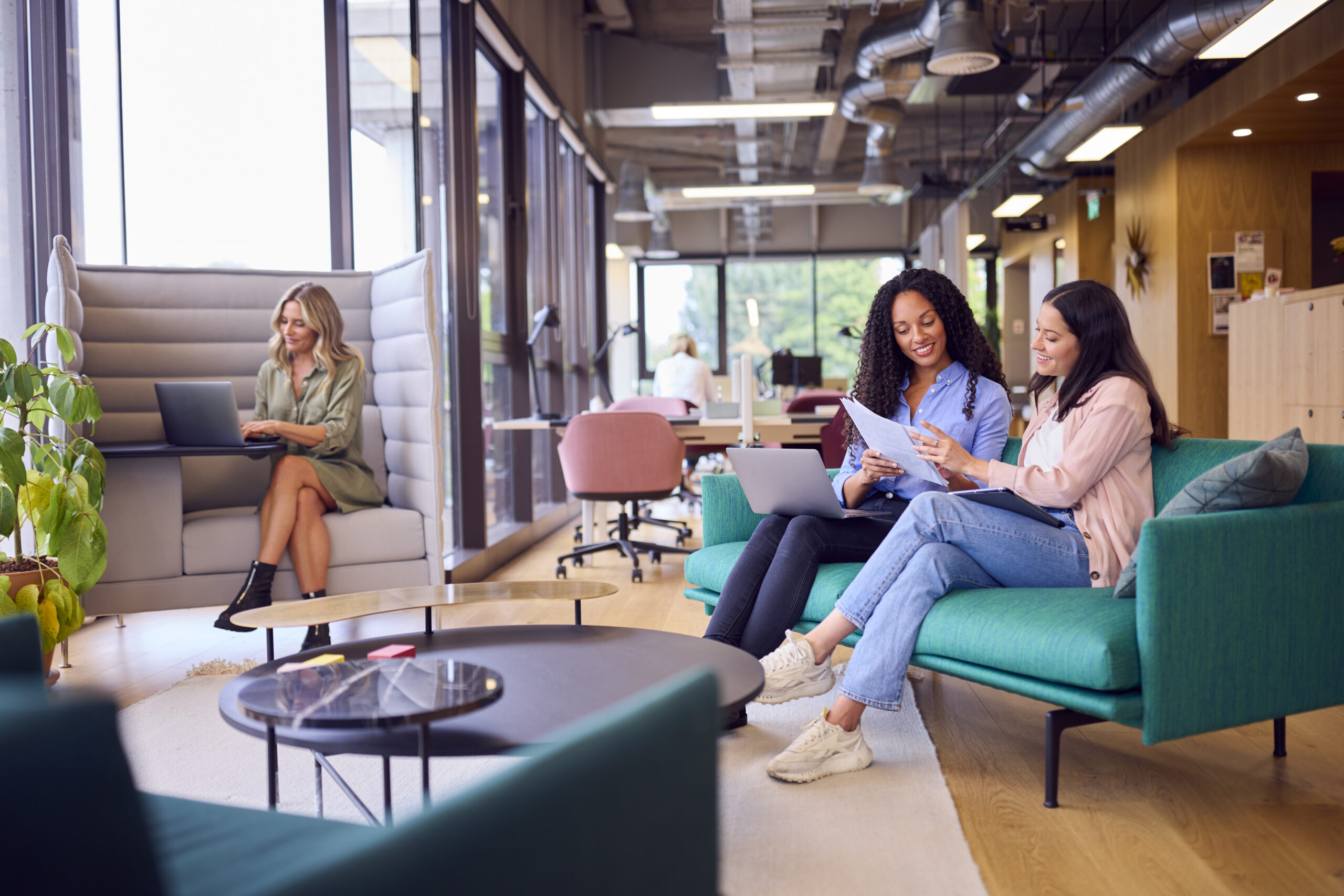 Businesswomen Having Informal Meeting In Breakout Seating Area Of Modern Office